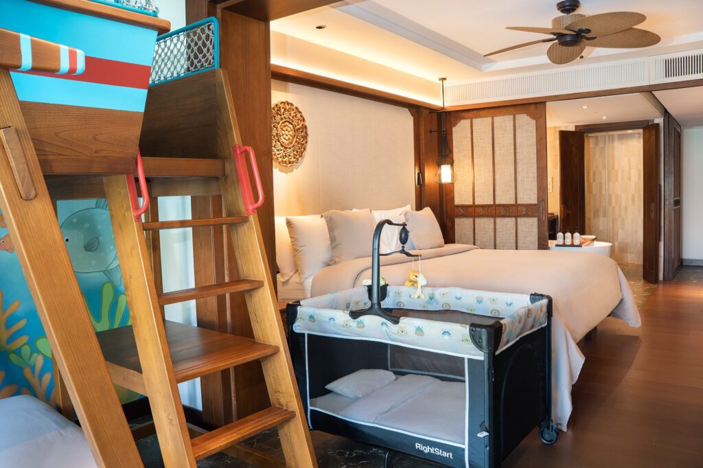 A baby cot set up beside the bed in a Family Concierge suite, with the boat-shaped bunk bed alongside