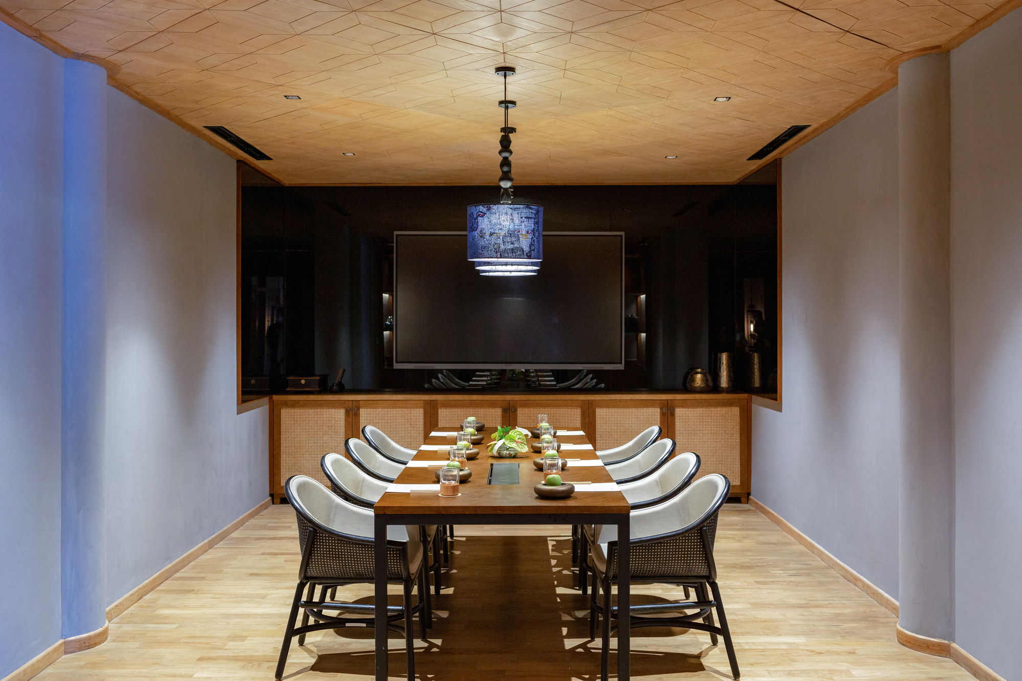 A private boardroom at Paradisus by Meliá Bali set for ten with a wall-mounted screen, rattan credenza and a blue pendant lamp