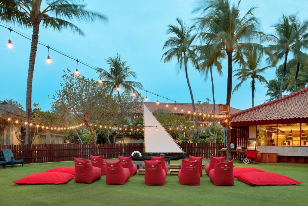 Red bean bags on the lawn facing an outdoor screen set in a boat, ready for family movie night at Paradisus by Meliá Bali