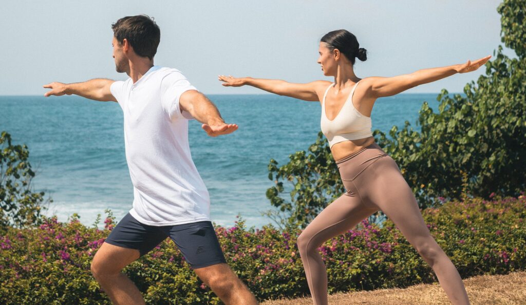 Two guests in a standing yoga pose on the clifftop lawn at Taman Surya, overlooking the ocean