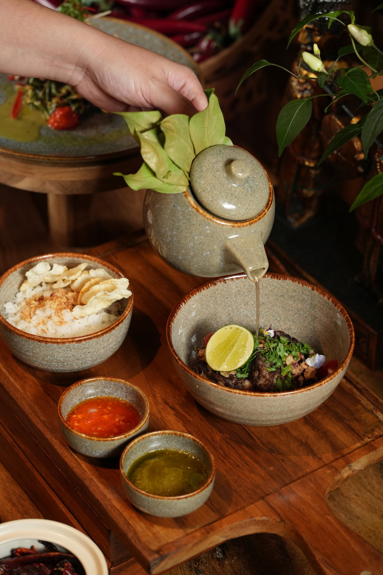 Broth poured from a ceramic teapot over a bowl of beef, lime and herbs, served with rice, crackers and two sambals at Malva, Paradisus by Melia Bali
