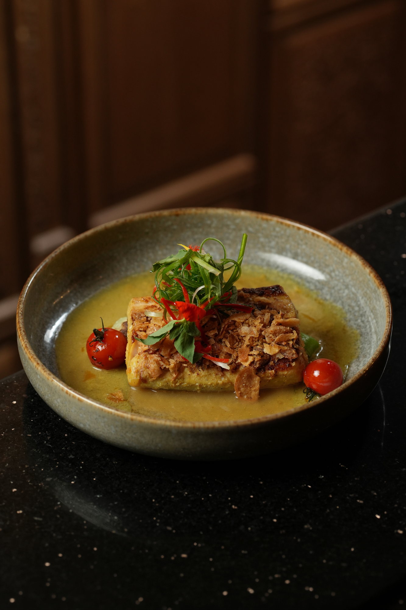 Seared fish in a yellow curry broth photographed against a dark ground at Malva, Paradisus by Melia Bali