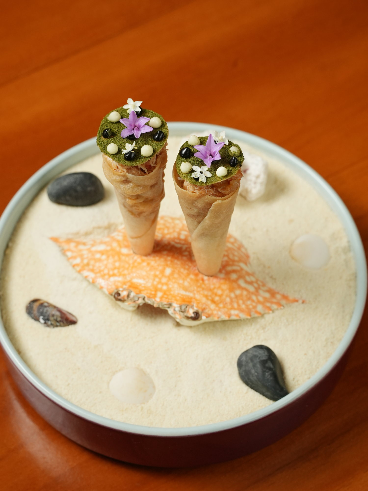 Two crab-filled cones standing in a bowl of sand with shells and pebbles at Peseta, Paradisus by Melia Bali