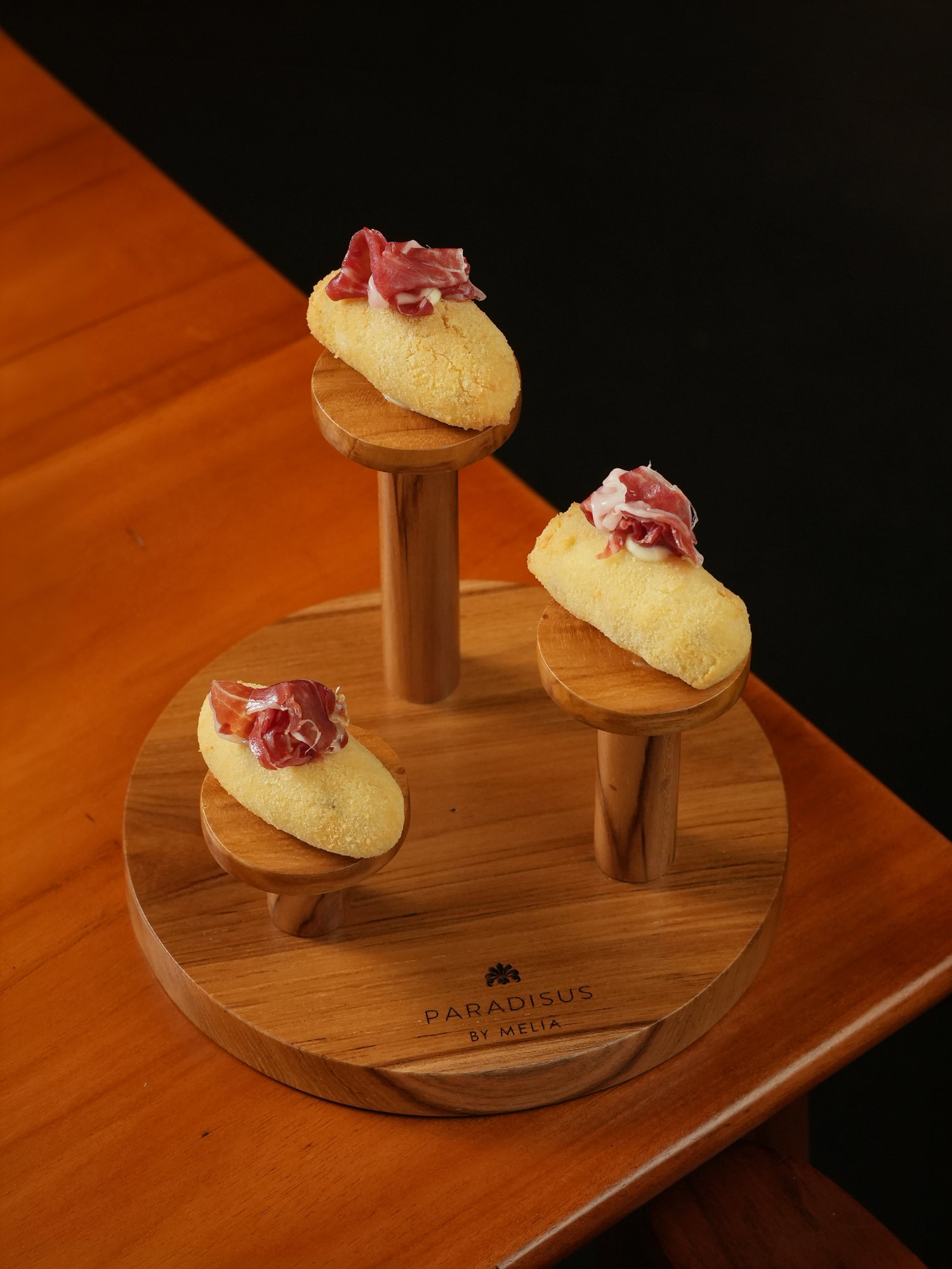 Three croquettes topped with jamon, served on a tiered wooden stand at Peseta, Paradisus by Melia Bali