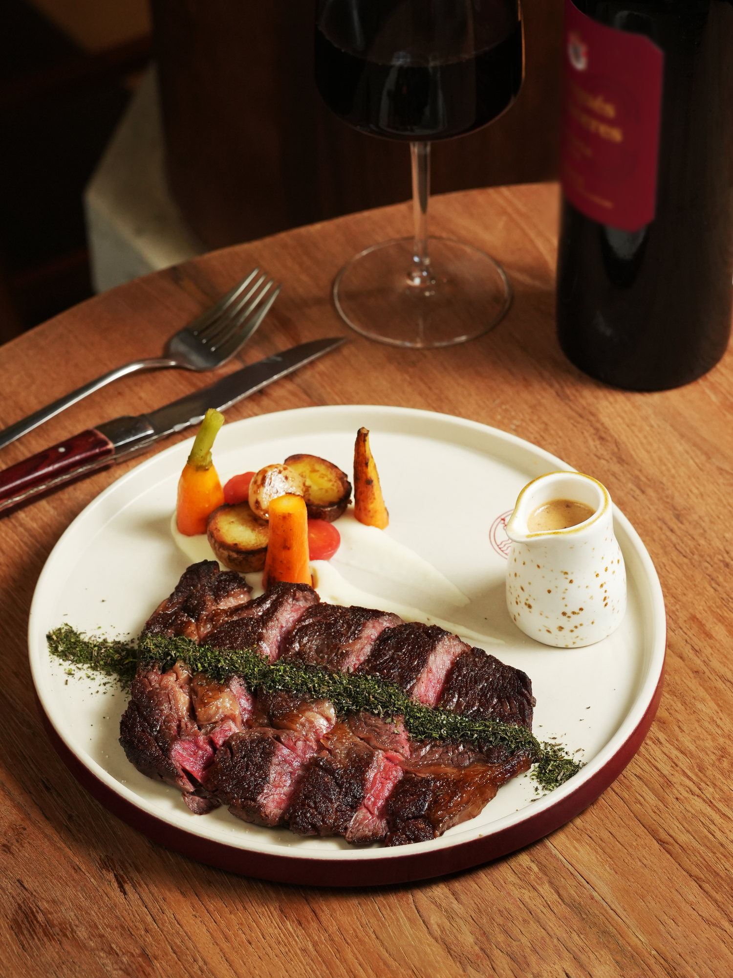 A sliced ribeye with herb crust, glazed carrots, roast potato and a jug of sauce at Peseta, Paradisus by Melia Bali