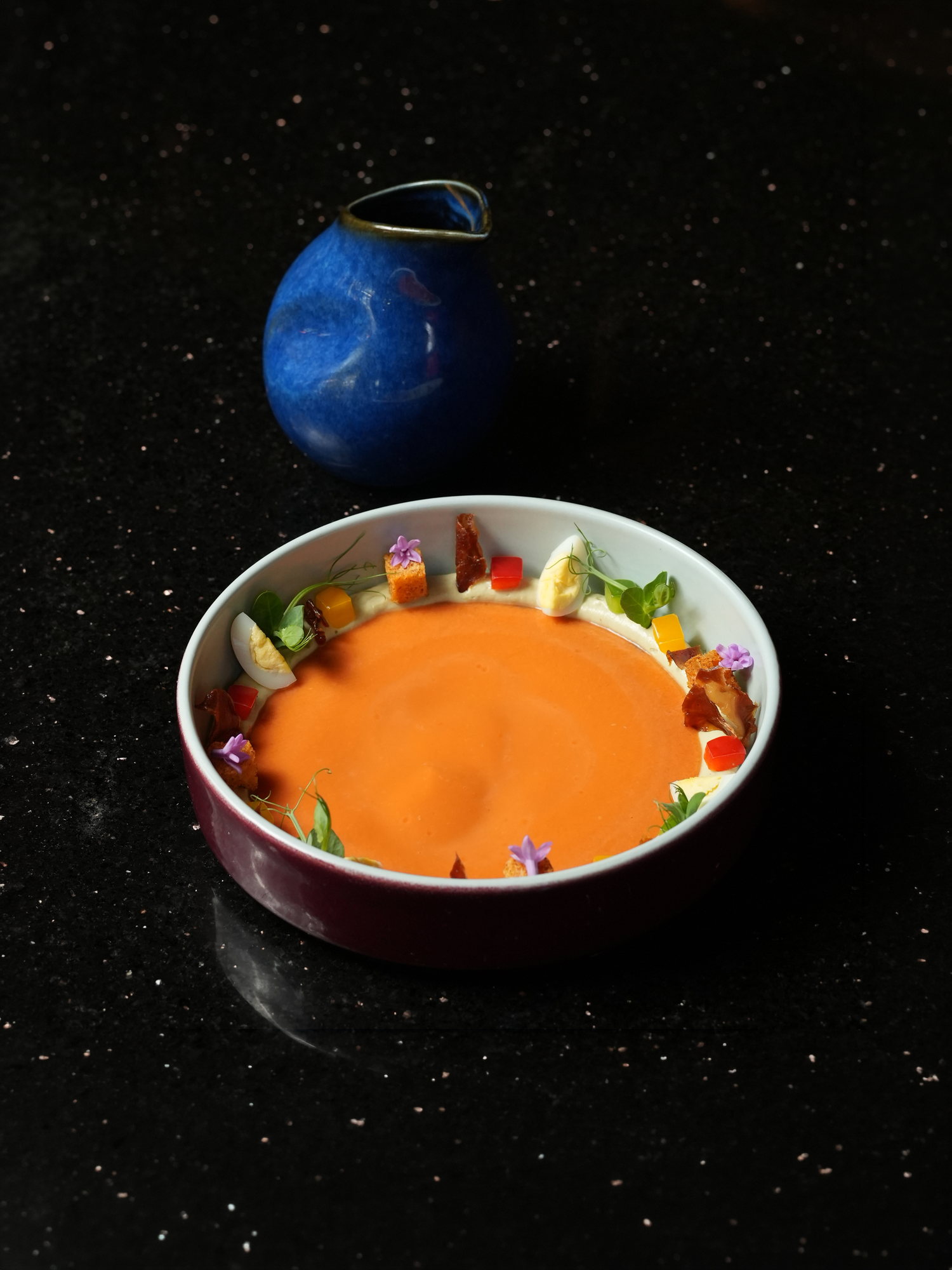 A chilled tomato soup ringed with quail egg, jamon, croutons and edible flowers at Peseta, Paradisus by Melia Bali