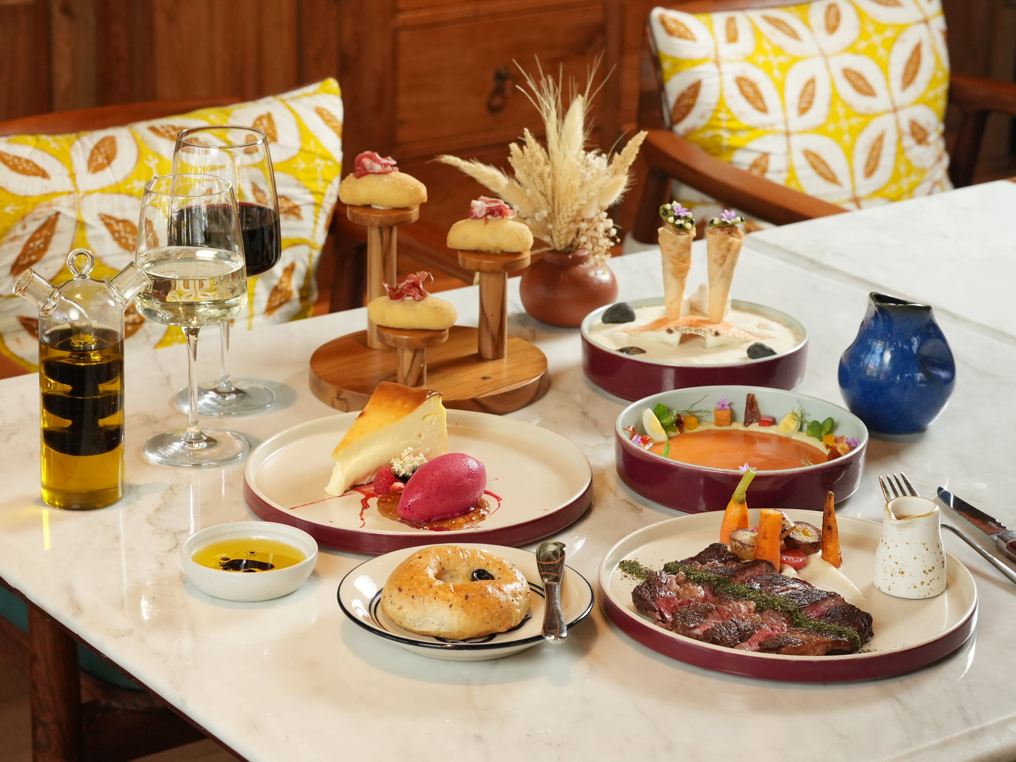 A table of Spanish dishes at Peseta, Paradisus by Melia Bali: croquettes with jamon, crab cones, salmorejo, cheesecake, ribeye and wine on a marble table