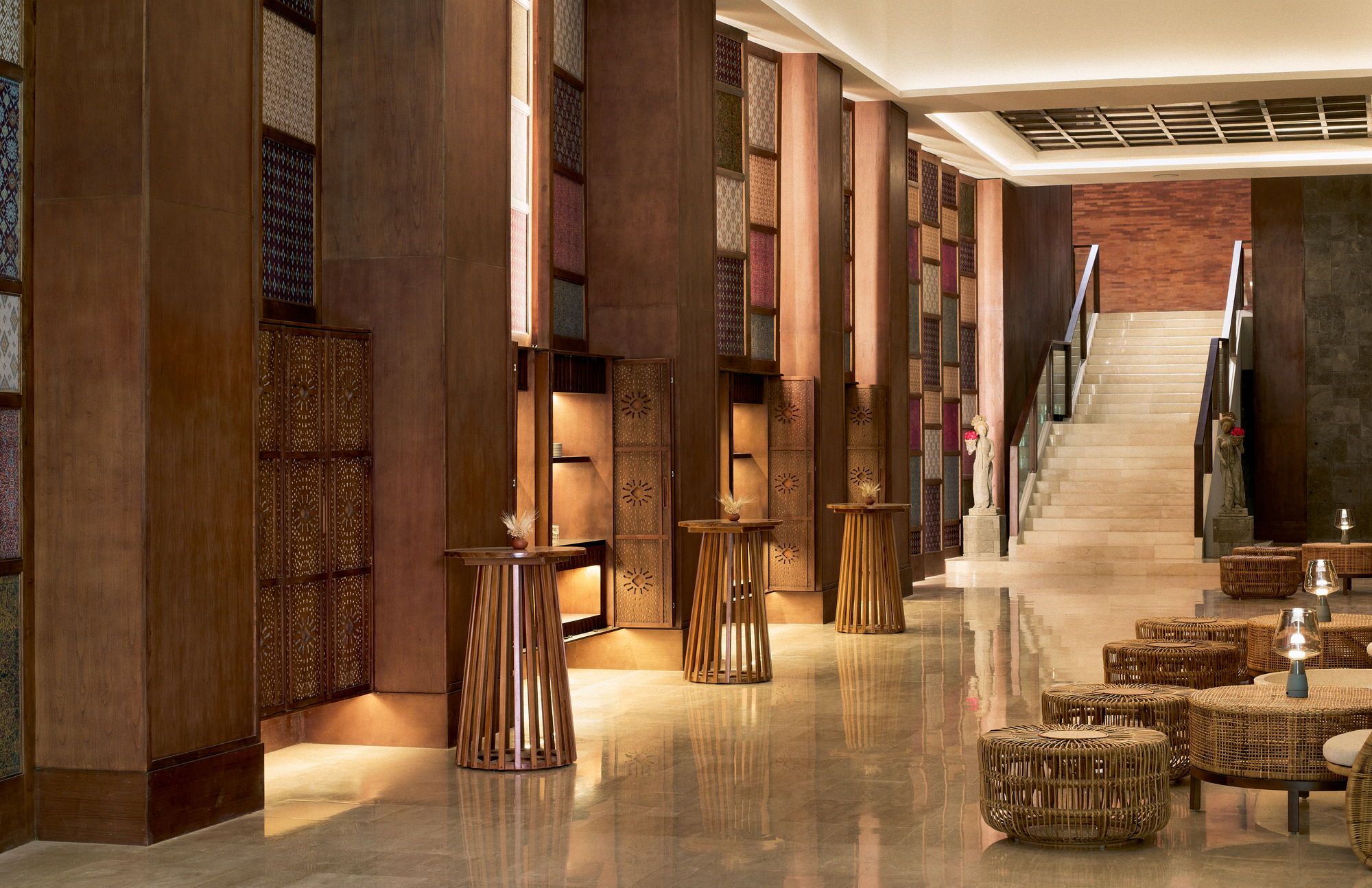 The ballroom foyer at Paradisus by Meliá Bali, a double-height space lined with framed Indonesian ikat panels, with cocktail tables and a stone staircase