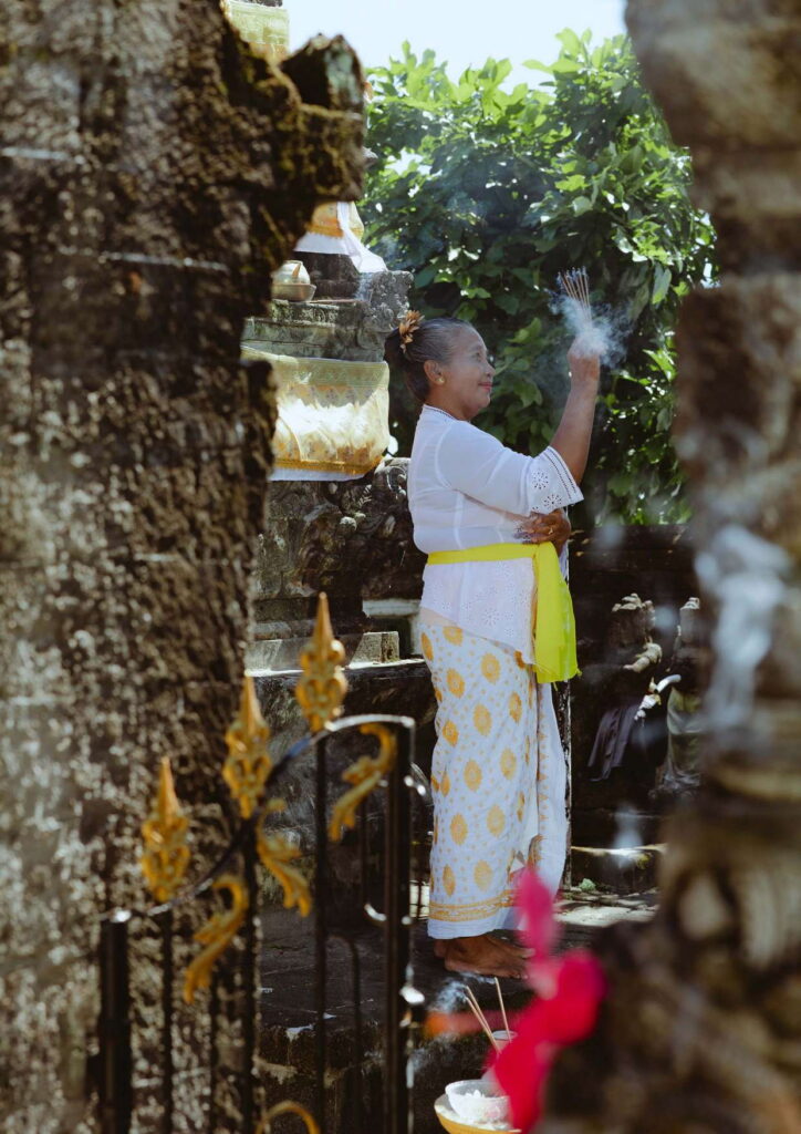 A Balinese woman in ceremonial dress raising incense at a temple shrine, the kind of offering made at a Balinese wedding blessing