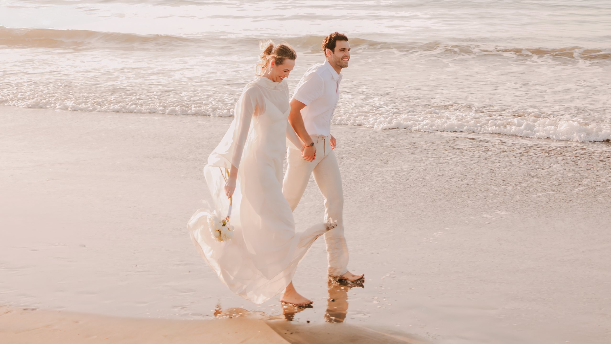 A bride and groom walking hand in hand along the shoreline at Paradisus by Meliá Bali in Nusa Dua