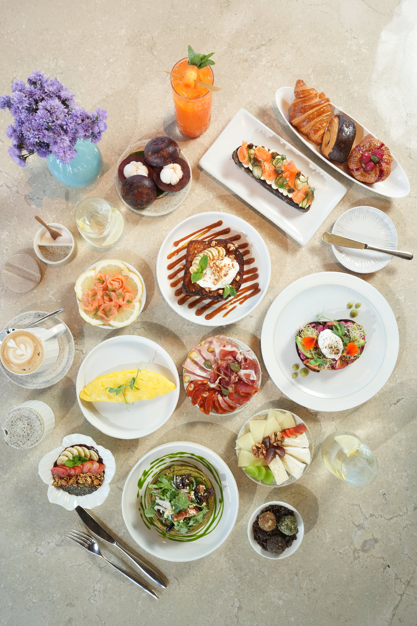 A breakfast table at Sante, Paradisus by Melia Bali: smoked salmon toast, French toast, an omelette, charcuterie, cheese, pastries, mangosteen and a carrot juice