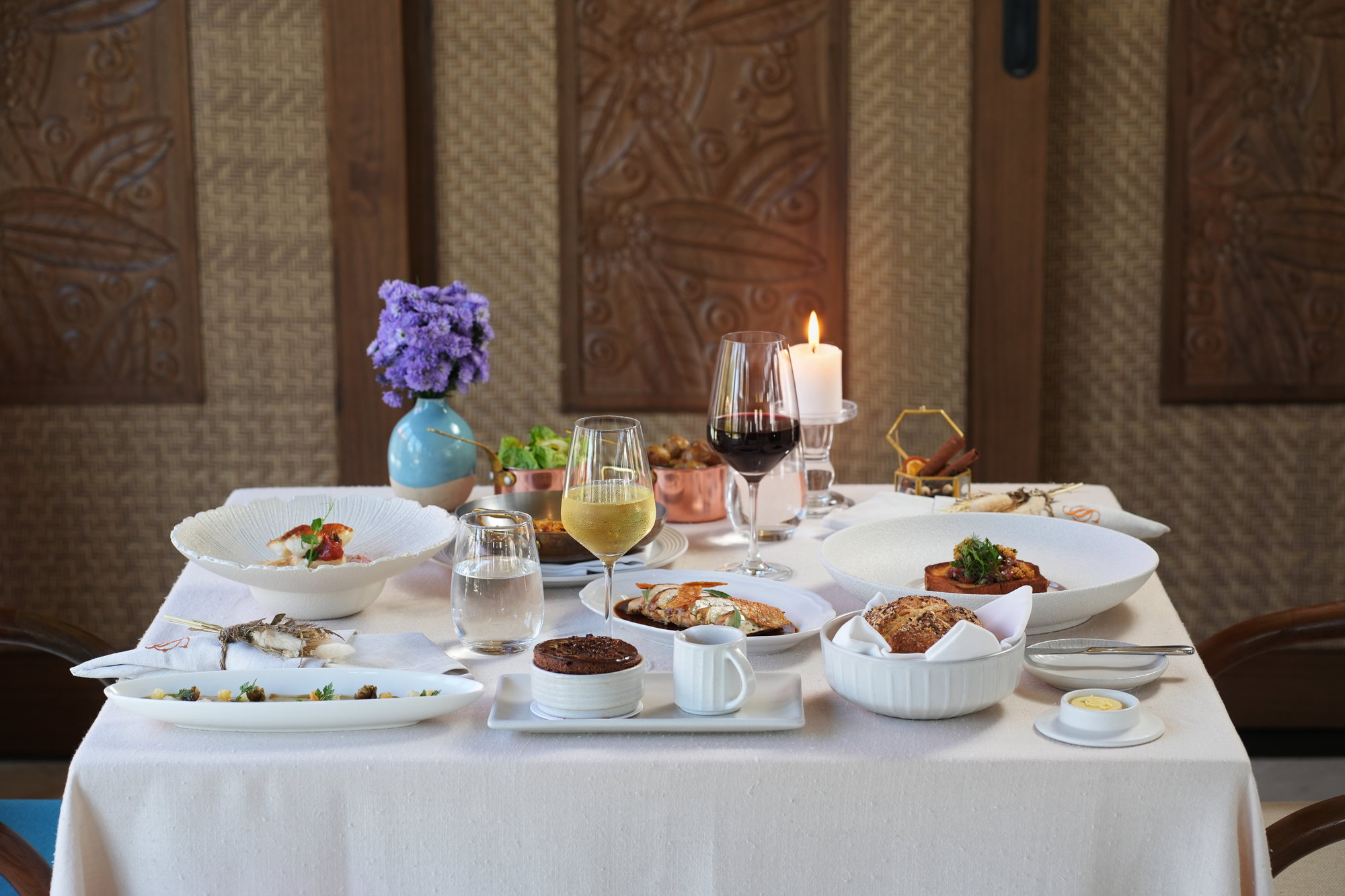 A dinner table at Sante, Paradisus by Melia Bali: carpaccio, steak tartare on brioche, seared fish, stuffed chicken, chocolate souffle, bread and wine, set against a carved Balinese screen