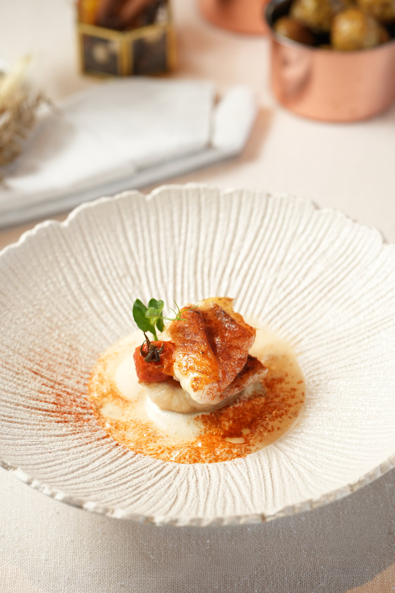 Crisp-skinned fish on a scallop with a paprika cream sauce, confit tomato and a caper berry, in a shell-shaped bowl at Sante, Paradisus by Melia Bali