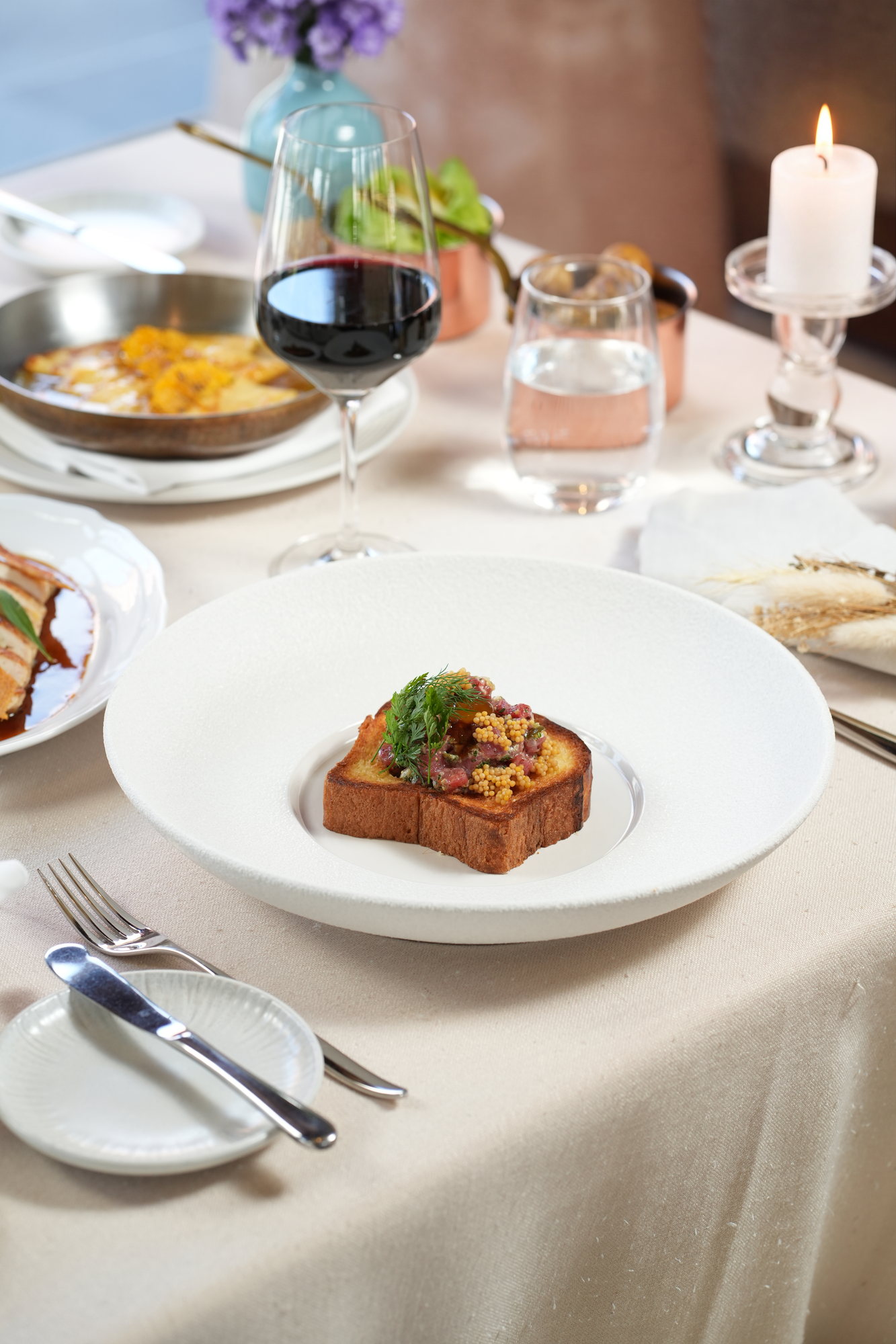 Steak tartare on toasted brioche at a candlelit table at Sante, Paradisus by Melia Bali, with red wine and crepes in a copper pan alongside