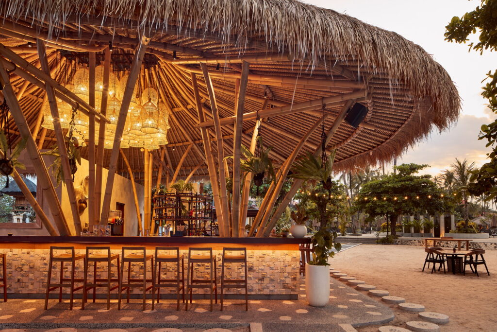 The Deck Beach Bar at Paradisus by Meliá Bali, a bamboo and thatch pavilion lit at sunset with bar stools facing the sand