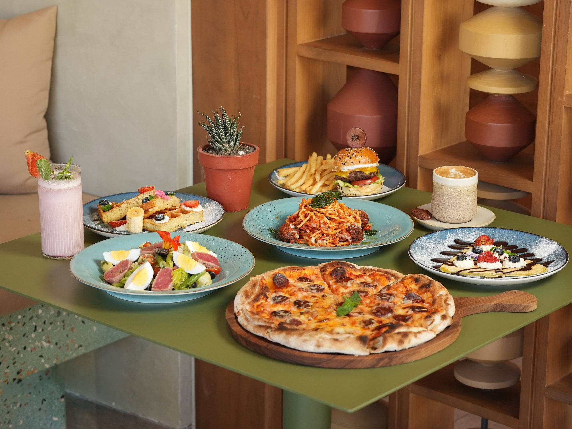 A table of dishes at The Shack, Paradisus by Melia Bali: waffles, a tuna nicoise salad, spaghetti and meatballs, a cheeseburger with fries, chorizo pizza, a crepe, a strawberry shake and a latte