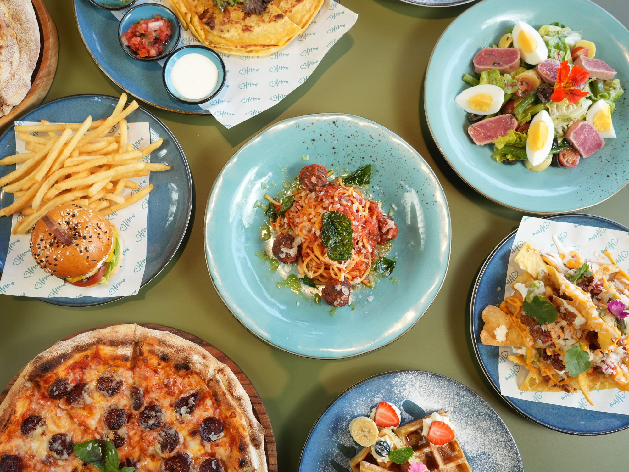 The same table at The Shack, Paradisus by Melia Bali, seen from above: quesadilla, spaghetti and meatballs, loaded nachos, tuna nicoise salad, waffles, burger with fries and chorizo pizza