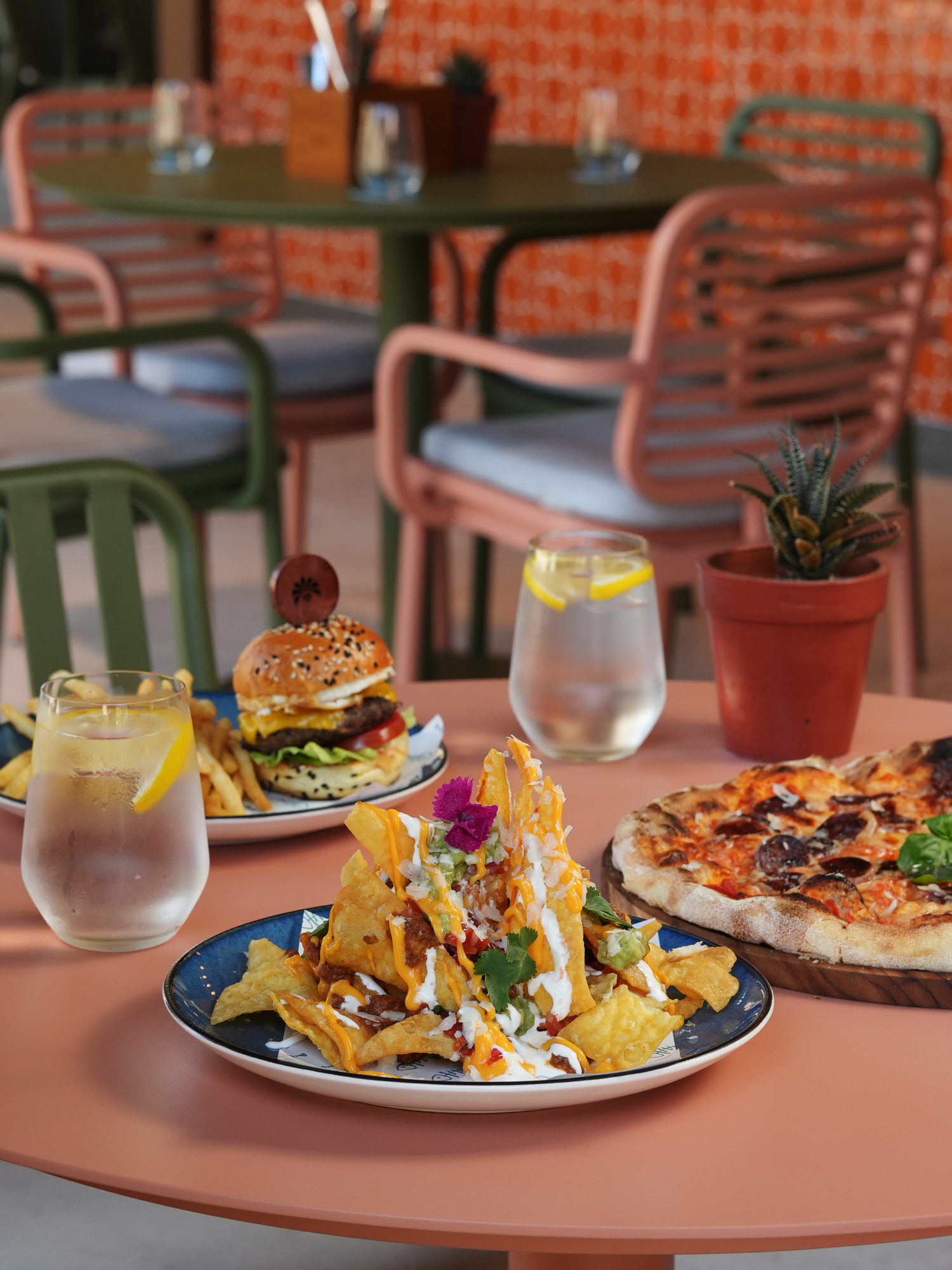 Loaded nachos, a cheeseburger with fries and a chorizo pizza on a terracotta table on The Shack terrace at Paradisus by Melia Bali