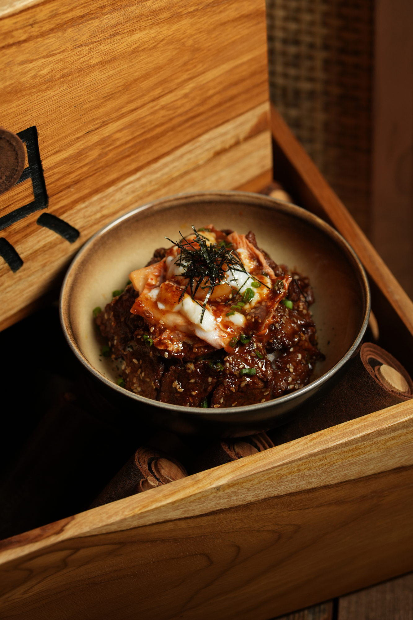 A rice bowl of glazed beef with kimchi, melted cheese, sesame and nori, served in a wooden box at Tokimeku, Paradisus by Melia Bali