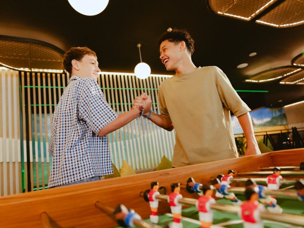 Two teenagers shaking hands over the table football at YOURWAY Teen Club, Paradisus by Meliá Bali