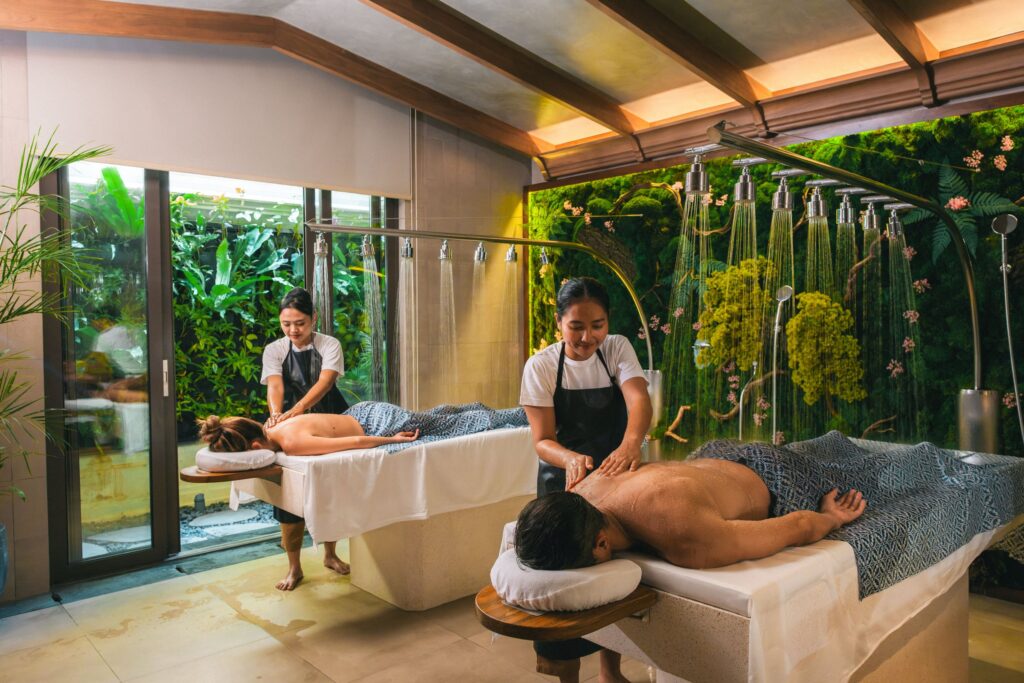 Two therapists giving a couples massage under a row of rain-shower heads at YHI Spa, Paradisus by Meliá Bali, beside a moss wall and a garden window