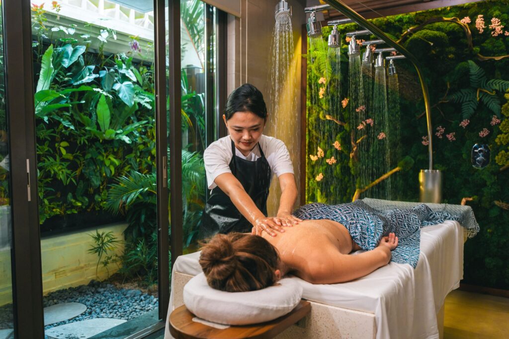 A therapist giving a massage beneath a rain-shower bar at YHI Spa, Paradisus by Meliá Bali, in front of a moss wall with pink flowers